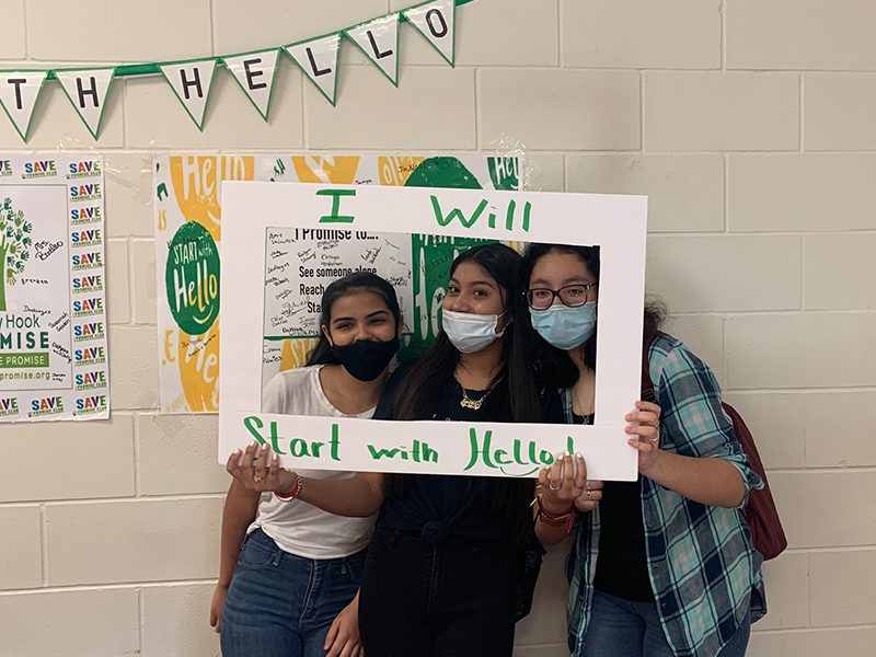 The image shows three students within a photo frame. The frames says “I will Start With Hello!"