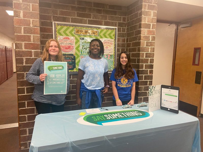 Three Seminole Middle School SAVE Promise Club students standing at a table promoting Say Something.